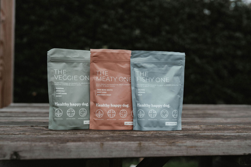 Three packages labeled 'The Veggie One', 'The Meaty One', and 'The Fishy One' on a wooden surface with a blurred natural background.